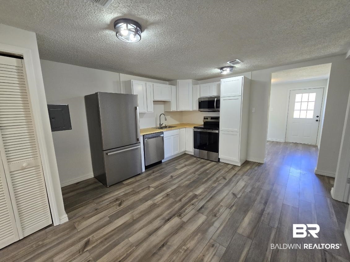 821 Dailey Street Brewton, AL 36426 - Photo 11 of 17 Kitchen featuring stainless steel appliances, white cabinetry, light countertops, dark wood-style flooring, and a textured ceiling