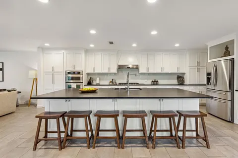 a kitchen with stainless steel appliances a stove a sink a refrigerator and white cabinets with wooden floor