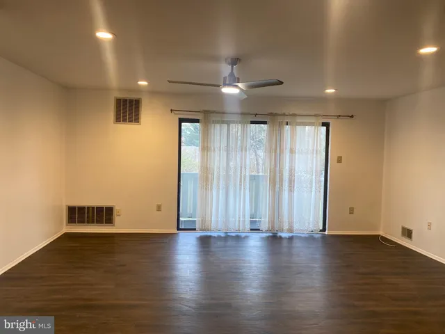 an empty room with wooden floor and windows with curtains