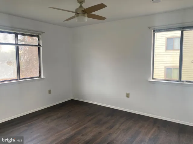an empty room with wooden floor fan and windows