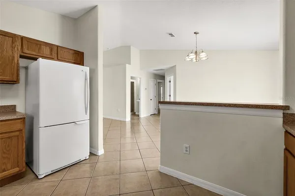 a view of a refrigerator in kitchen and an empty room with wooden floor