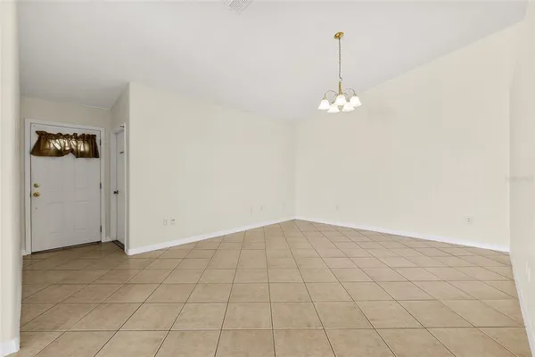 an empty room with kitchen view and a chandelier fan