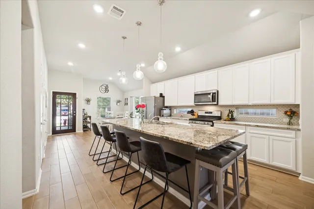 a kitchen with stainless steel appliances kitchen island granite countertop a dining table chairs and white cabinets