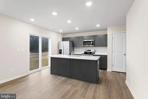 a large kitchen with stainless steel appliances granite countertop a large counter top a wooden floors and a large window
