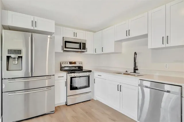 a kitchen with stainless steel appliances granite countertop white cabinets a sink a stove a refrigerator and white cabinets