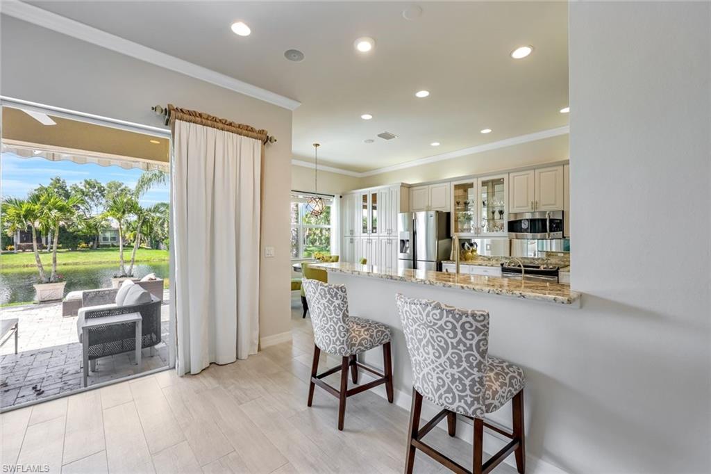 6582 Monterey Point Naples, FL 34105 - Photo 10 of 28 Kitchen with light stone counters, glass insert cabinets, ornamental molding, a kitchen breakfast bar, and recessed lighting