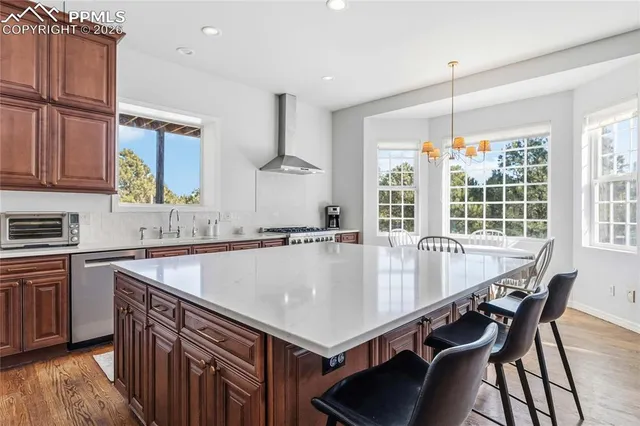 a kitchen with stainless steel appliances granite countertop a white stove top oven a sink a dining table and chairs with wooden floor