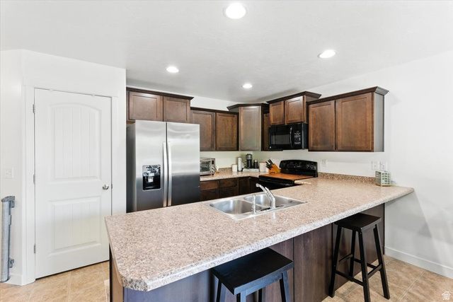 1187 Seraphim Court Layton, UT 84041 - Photo 5 of 18 Kitchen with a kitchen breakfast bar, dark wood finish cabinetry, black appliances, a peninsula, and light countertops