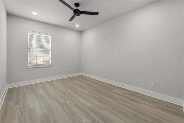 an empty room with wooden floor ceiling fan and windows