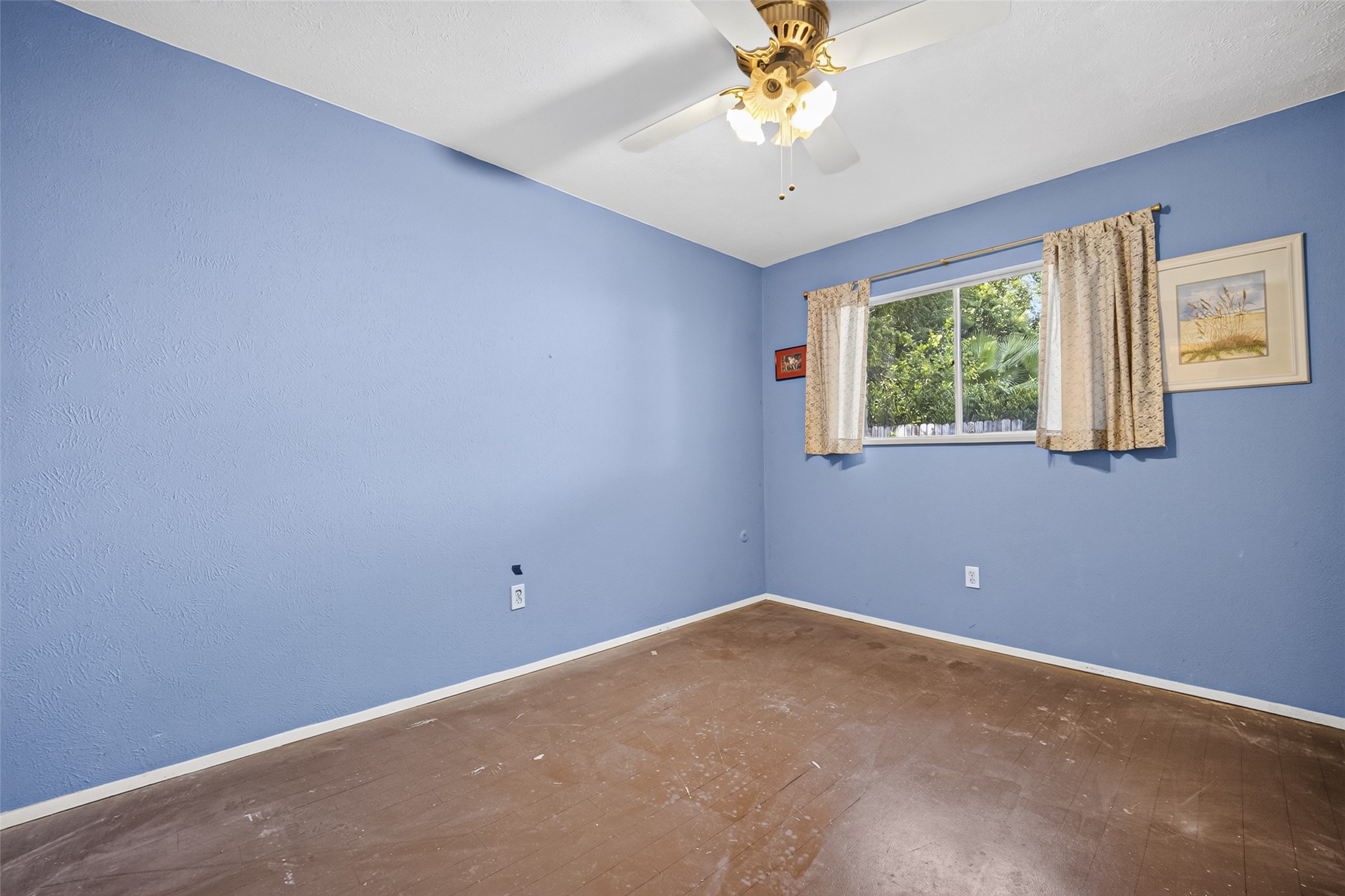 22926 Millgate Drive Spring, TX 77373 - Photo 20 of 34 This room features blue walls and a ceiling fan. It has a large window with curtains, providing natural light and a view of greenery outside. The space is unfurnished with a bare floor, ready for customization.