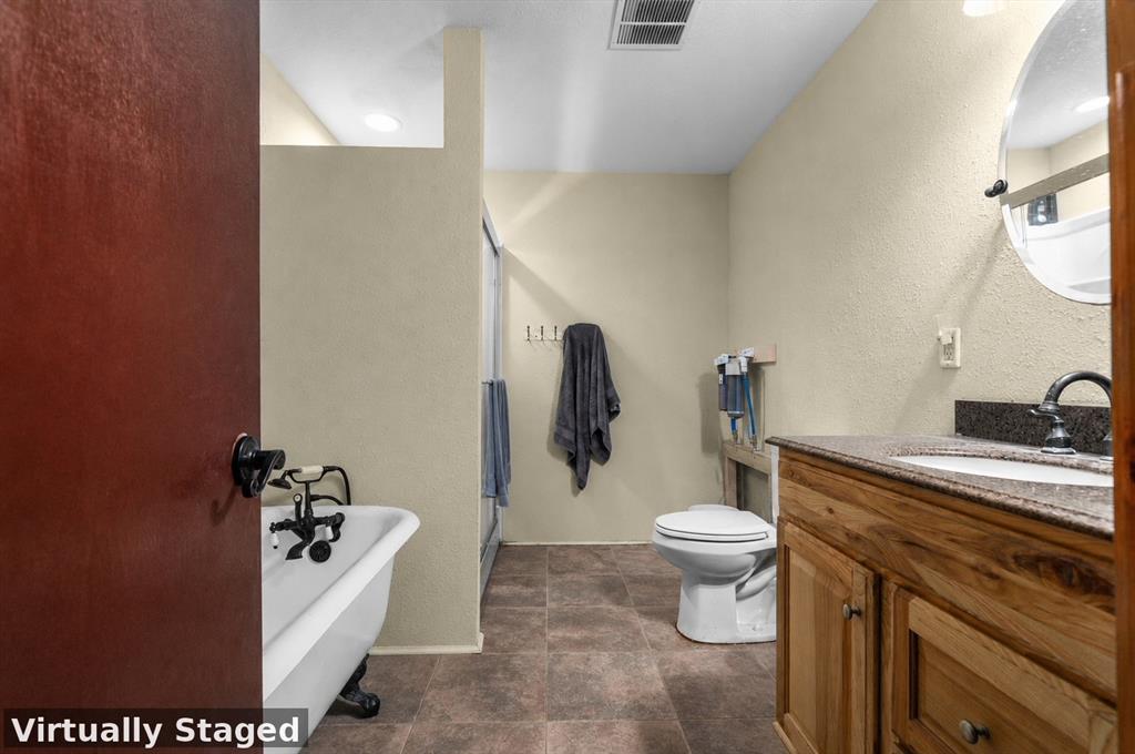 3216 Old Ewing Road Lufkin, TX 75901 - Photo 17 of 24 Bathroom featuring a clawfoot tub with dark-finish fixtures, a wood vanity with a light-toned countertop and integrated sink, a toilet, and brown-toned tile flooring