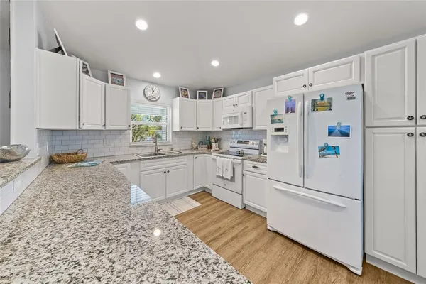 a large kitchen with stainless steel appliances granite countertop a refrigerator a stove a sink dishwasher and white cabinets with wooden floor