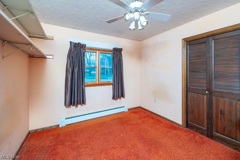 4251 Seville Road Seville, OH 44273 - Photo 12 of 20 Unfurnished bedroom featuring ceiling fan, a baseboard heating unit, dark carpet, a closet, and a textured ceiling