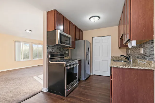 a kitchen with stainless steel appliances granite countertop a stove a sink dishwasher a refrigerator and a microwave oven with wooden floor