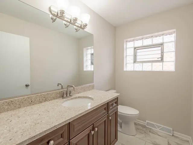 a bathroom with a granite countertop sink a toilet and a window