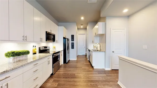 a large kitchen with stainless steel appliances kitchen island granite countertop a refrigerator a stove a sink dishwasher and white cabinets with wooden floor