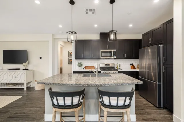 a kitchen with stainless steel appliances kitchen island granite countertop a refrigerator a stove a sink a dining table and chairs with wooden floor
