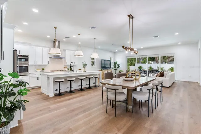 a kitchen with kitchen island stainless steel appliances a table chairs sink and stove top oven