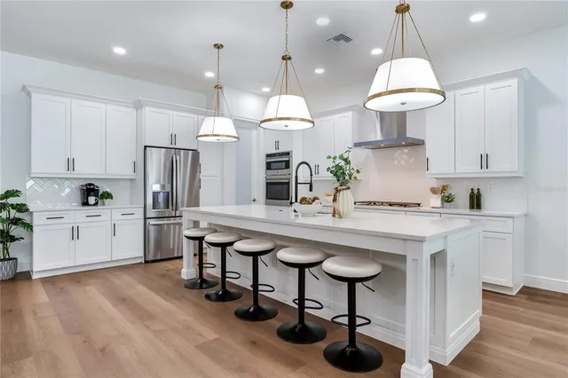 a large white kitchen with lots of counter space dining table and stainless steel appliances