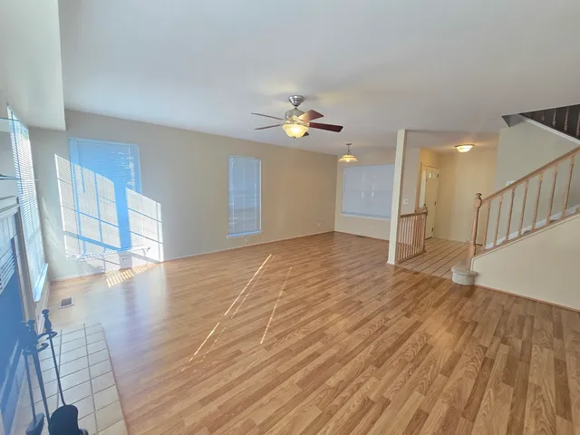a view of an empty room with wooden floor and a ceiling fan