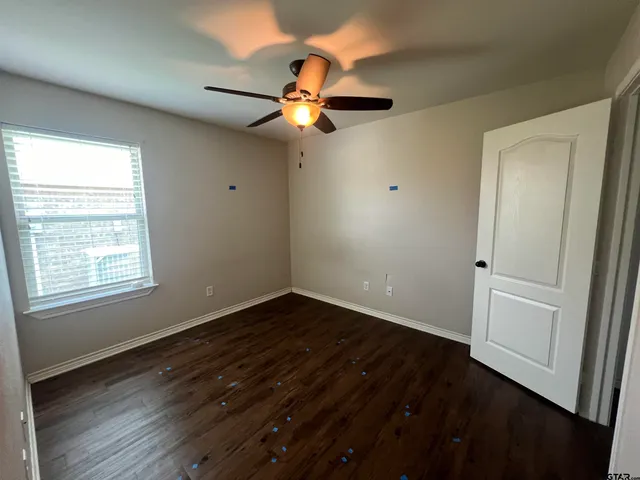 an empty room with wooden floor fan and windows