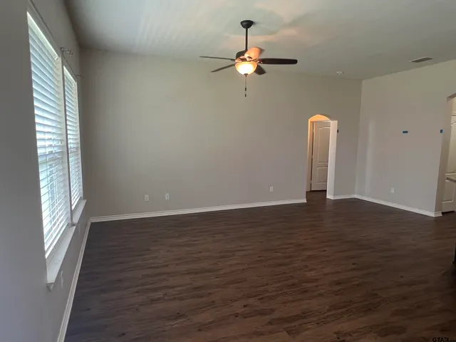 an empty room with wooden floor chandelier fan and windows