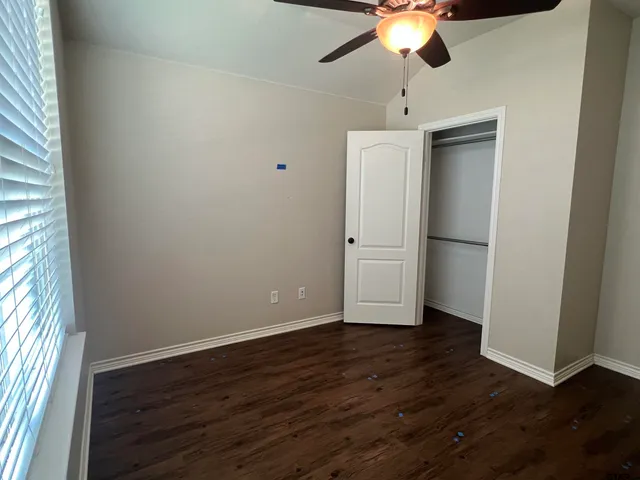 an empty room with wooden floor chandelier fan and windows