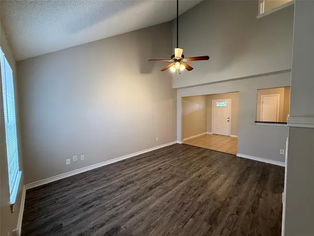 an empty room with wooden floor chandelier fan and windows