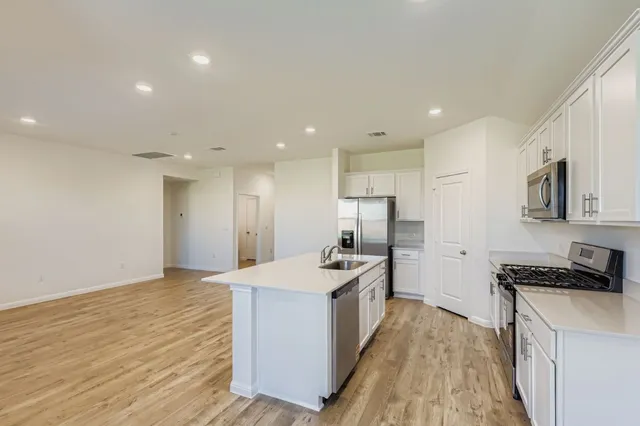 a view of kitchen with granite countertop refrigerator oven a sink and white cabinets with wooden floor
