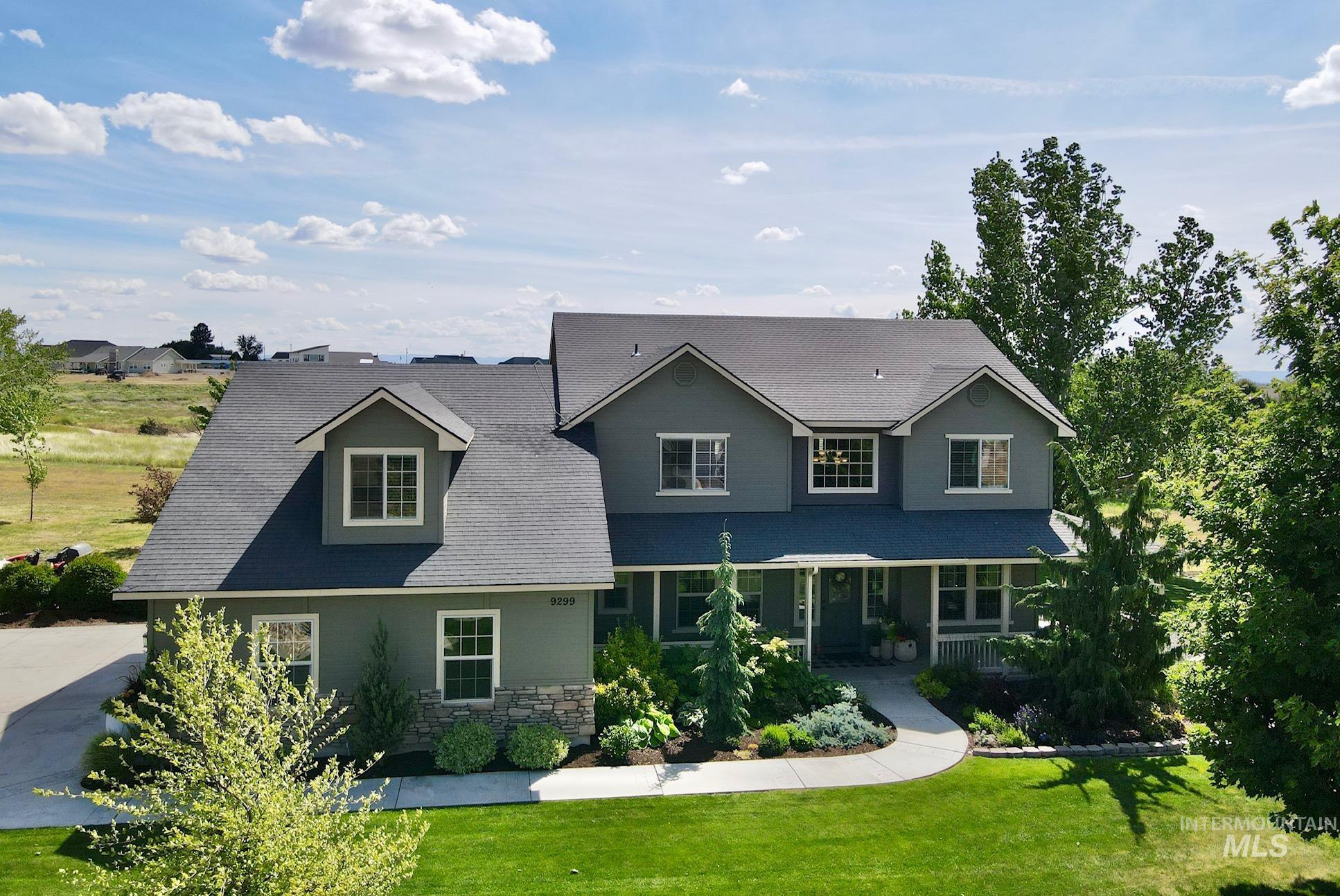 9299 Kemp Road Middleton, ID 83644 - Photo 1 of 50 Two-story residence featuring a gray exterior with stone accents, a covered front porch, a curved concrete pathway, a manicured lawn, and mature landscaping