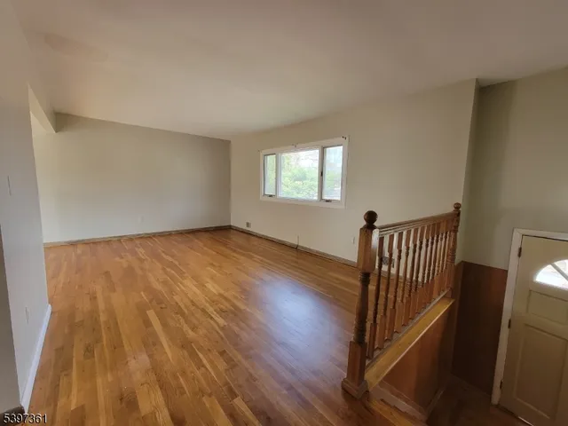 a view of empty room with wooden floor and kitchen
