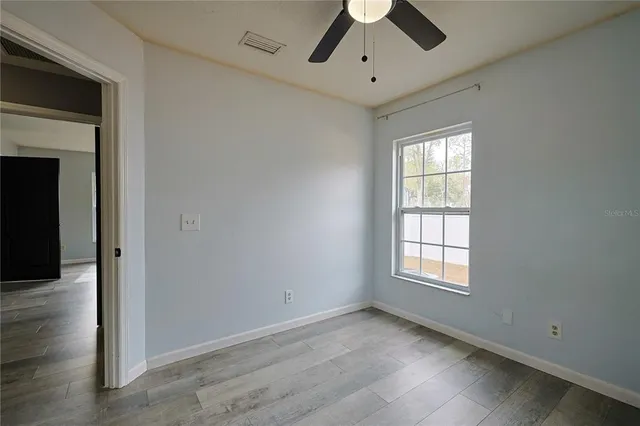 an empty room with chandelier fan and windows
