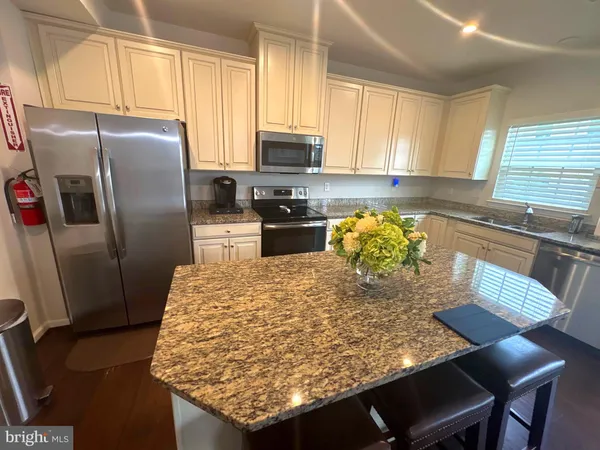 a kitchen with granite countertop a refrigerator a stove a sink dishwasher and white cabinets with wooden floor