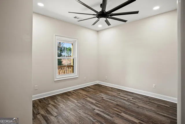 an empty room with wooden floor ceiling fan and windows