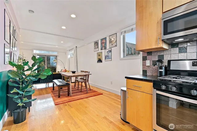 a kitchen with stainless steel appliances a stove a sink a microwave a dining table and chairs with wooden floor