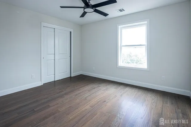 an empty room with wooden floor ceiling fan and windows