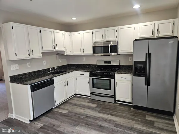 a white kitchen with granite countertop a stove a sink and white cabinets