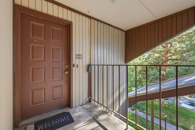 1175 Canyon Road, Unit 86 Ogden, UT 84404 - Photo 5 of 29 Entry door with multiple panels, exterior wall with vertical siding, outdoor balcony with metal railing, and tree-lined backdrop