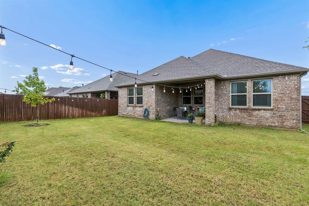 10313 Geode Street Aubrey, TX 76227 - Photo 12 of 13 Spacious backyard featuring a covered patio, string lighting, mature perimeter fencing, and a manicured lawn