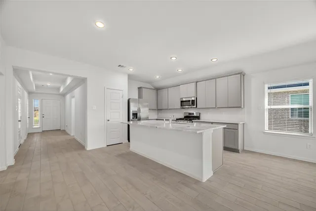 a large white kitchen with stainless steel appliances granite countertop a stove a sink a refrigerator white cabinets and wooden floor