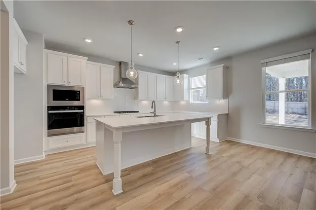 a kitchen with stainless steel appliances kitchen island granite countertop a stove a sink and white cabinets with wooden floor