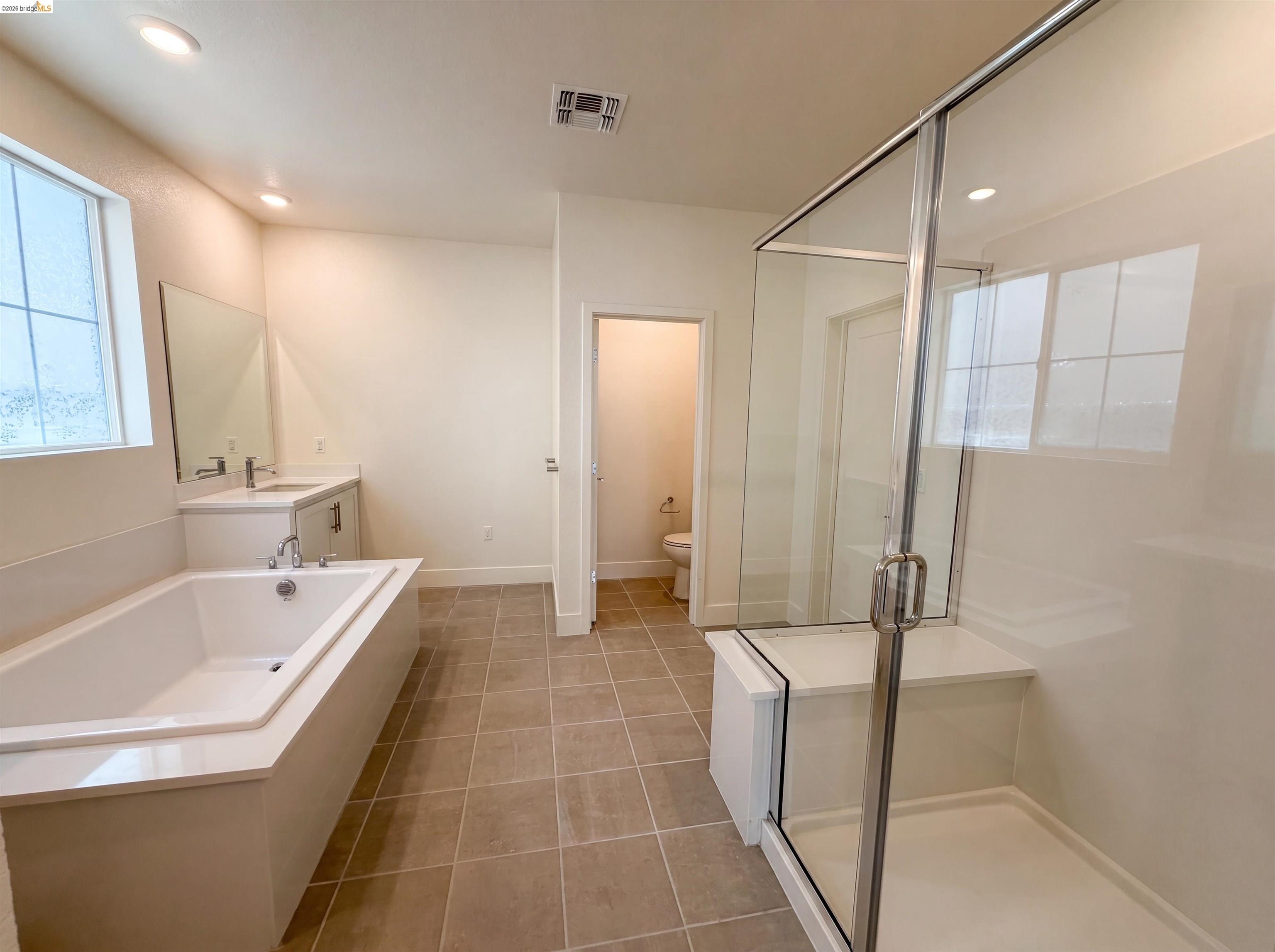 9034 Rudder Way Newark, CA 94560 - Photo 10 of 38 Spacious bathroom featuring a built-in soaking tub with a surrounding deck, a separate glass-enclosed shower with a bench, a single vanity with a solid surface countertop, and large format tile flooring