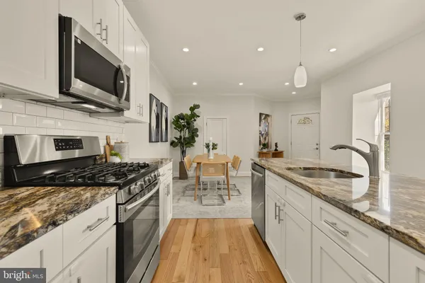 a kitchen with stainless steel appliances granite countertop a stove top oven a sink dishwasher a dining table and chairs with wooden floor