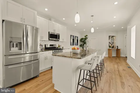 a kitchen with stainless steel appliances kitchen island granite countertop a refrigerator a stove a sink a dining table and chairs with wooden floor