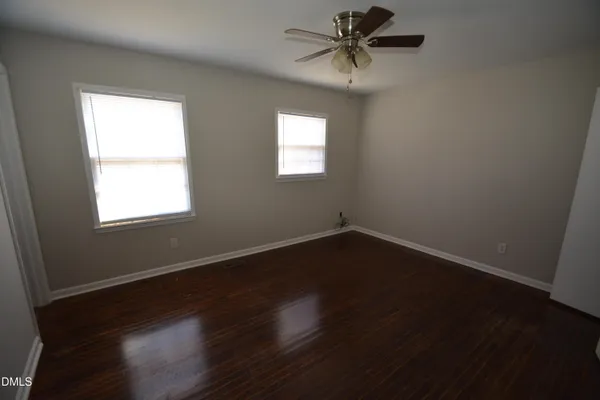 an empty room with wooden floor fan and windows
