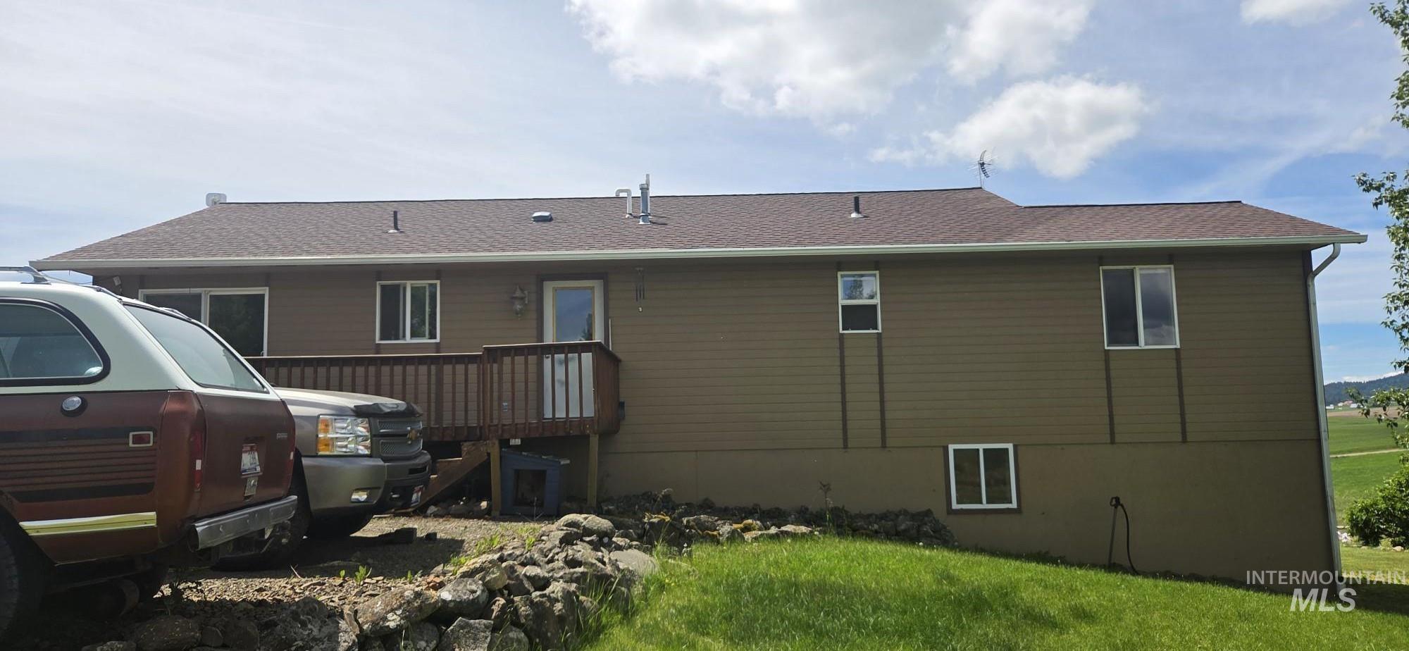394 Substation Road Cottonwood, ID 83522 - Photo 5 of 37 Green siding exterior with a brown shingle roof, white window frames, and an elevated wood deck
