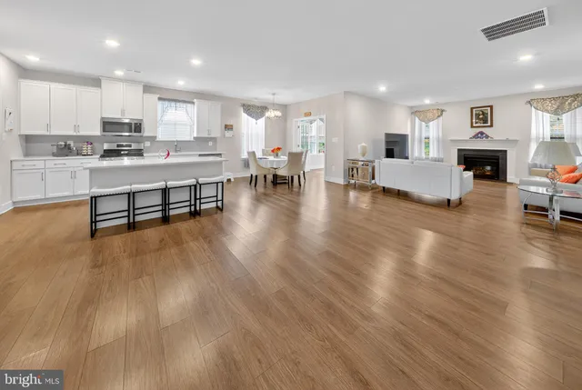 a living room with stainless steel appliances furniture wooden floor and a kitchen view