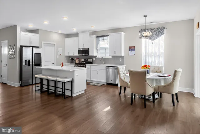 a kitchen with a dining table chairs wooden floor appliances and cabinets