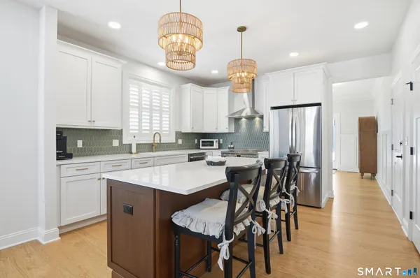 a kitchen with stainless steel appliances kitchen island granite countertop a dining table chairs and white cabinets