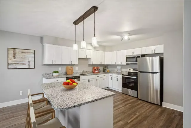 a kitchen with stainless steel appliances granite countertop a refrigerator a stove a sink dishwasher and white cabinets with wooden floor